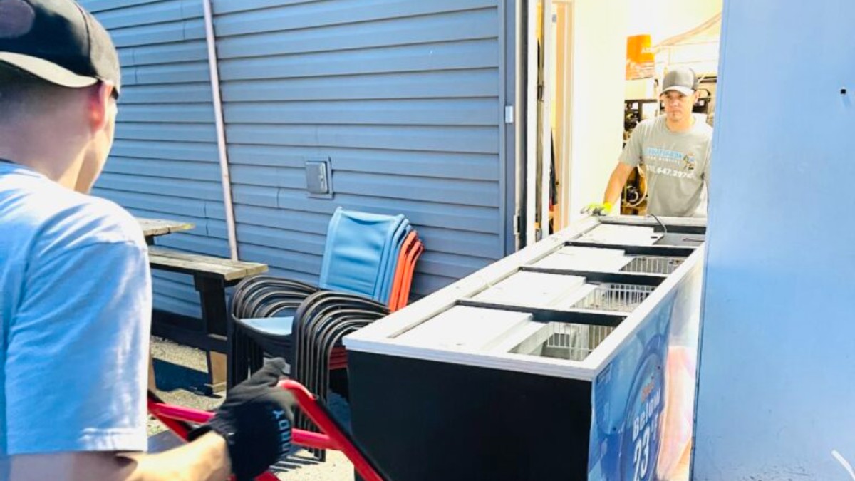 Clutter Box crew members wheeling a commercial refrigeration unit out on a dolly during an appliance removal in Butler County, Ohio