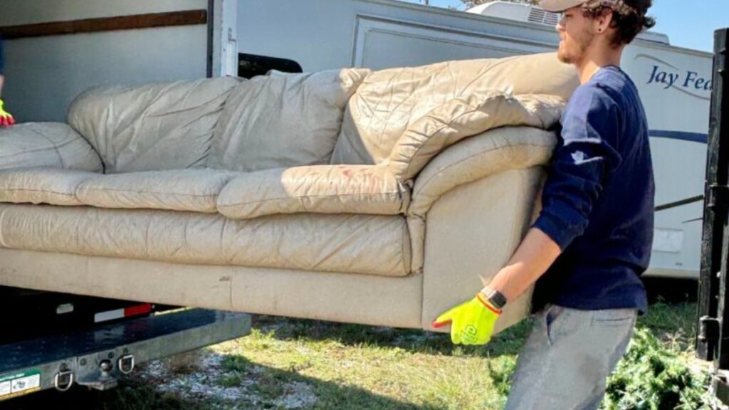 A Clutter Box crew member carrying an old leather sofa into a box truck during a furniture removal in West Chester, Ohio