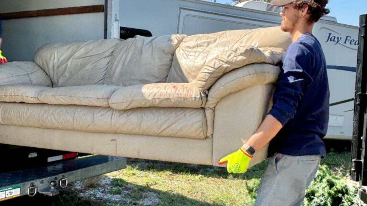 A Clutter Box crew member carrying an old leather sofa into a box truck during a furniture removal in West Chester, Ohio